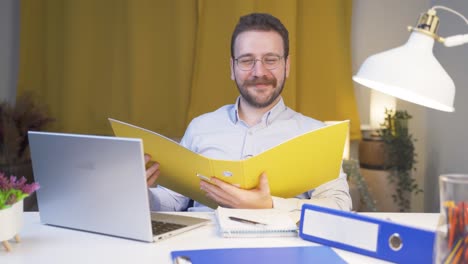 Home-office-worker-man-smiling-at-camera-looking-at-paperwork.